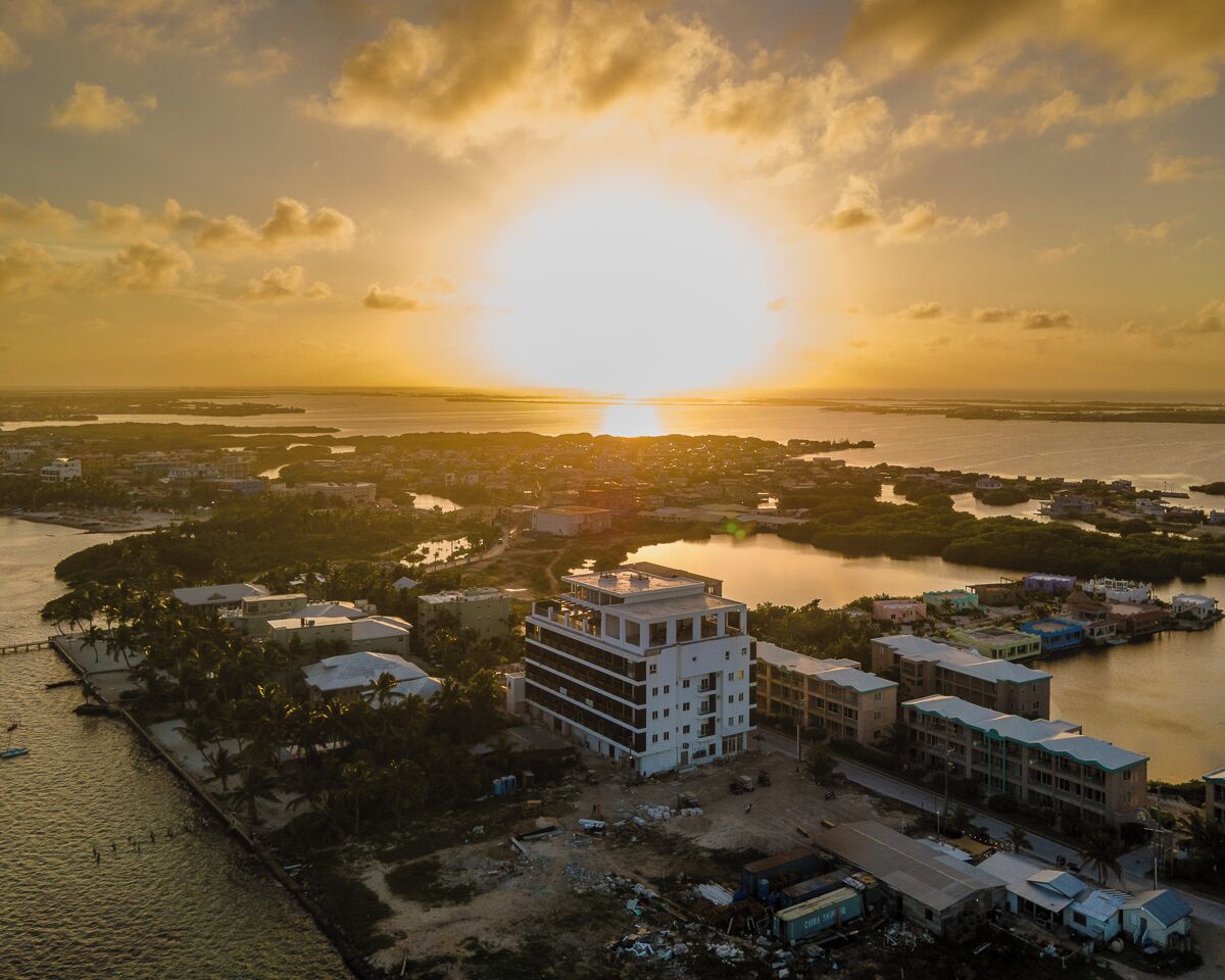 An aerial view of a coastal cityscape during sunset with buildings, water bodies, and a clear sky.