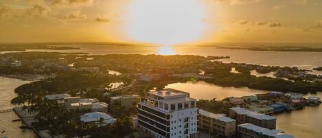 An aerial view of a coastal cityscape during sunset with buildings, water bodies, and a clear sky.