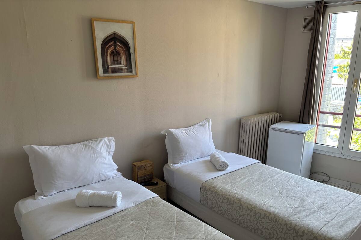A hotel room with two beds, a radiator, a small wooden nightstand, and a framed picture on the wall.