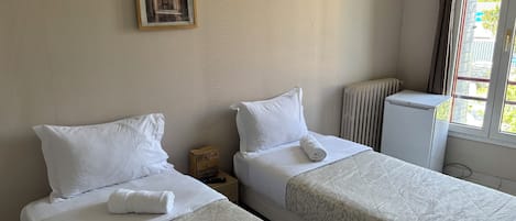 A hotel room with two beds, a radiator, a small wooden nightstand, and a framed picture on the wall.