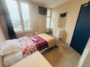 A bedroom with a bed, a bedside table, a window, a TV, a sink, and a mirror. - Le Grand Café (Châtillon)
