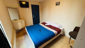 Een slaapkamer met een bed, nachtkastje, stoel, televisie en een badkamer met een wastafel en spiegel.