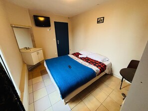 A bedroom with a bed, a bedside table, a chair, a TV, and a bathroom with a sink and mirror. - Le Grand Café (Châtillon)
