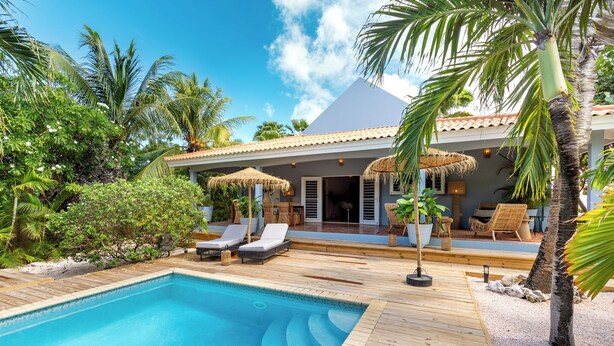 A poolside area with a wooden deck, lounge chairs, and a thatched umbrella. - Little Bali Curaçao: Exotic Caribbean Oasis (Grote Berg)