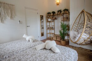 Een slaapkamer met twee bedden, een hangstoel, een wandplank met planten en een deur.