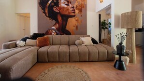 A modern living room with a large sectional sofa, a round coffee table, and a wall-mounted lamp. - Little Bali Curaçao: Exotic Caribbean Oasis (Grote Berg)
