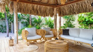 A covered outdoor seating area with wicker furniture and a woven ottoman. - Little Bali Curaçao: Exotic Caribbean Oasis (Grote Berg)