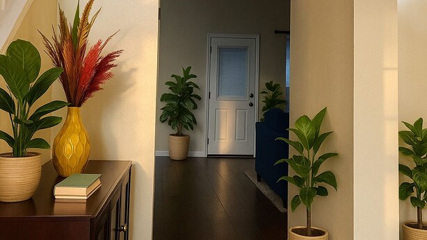 Un couloir avec un escalier sur la gauche, une porte au fond et des plantes en pot de chaque côté.