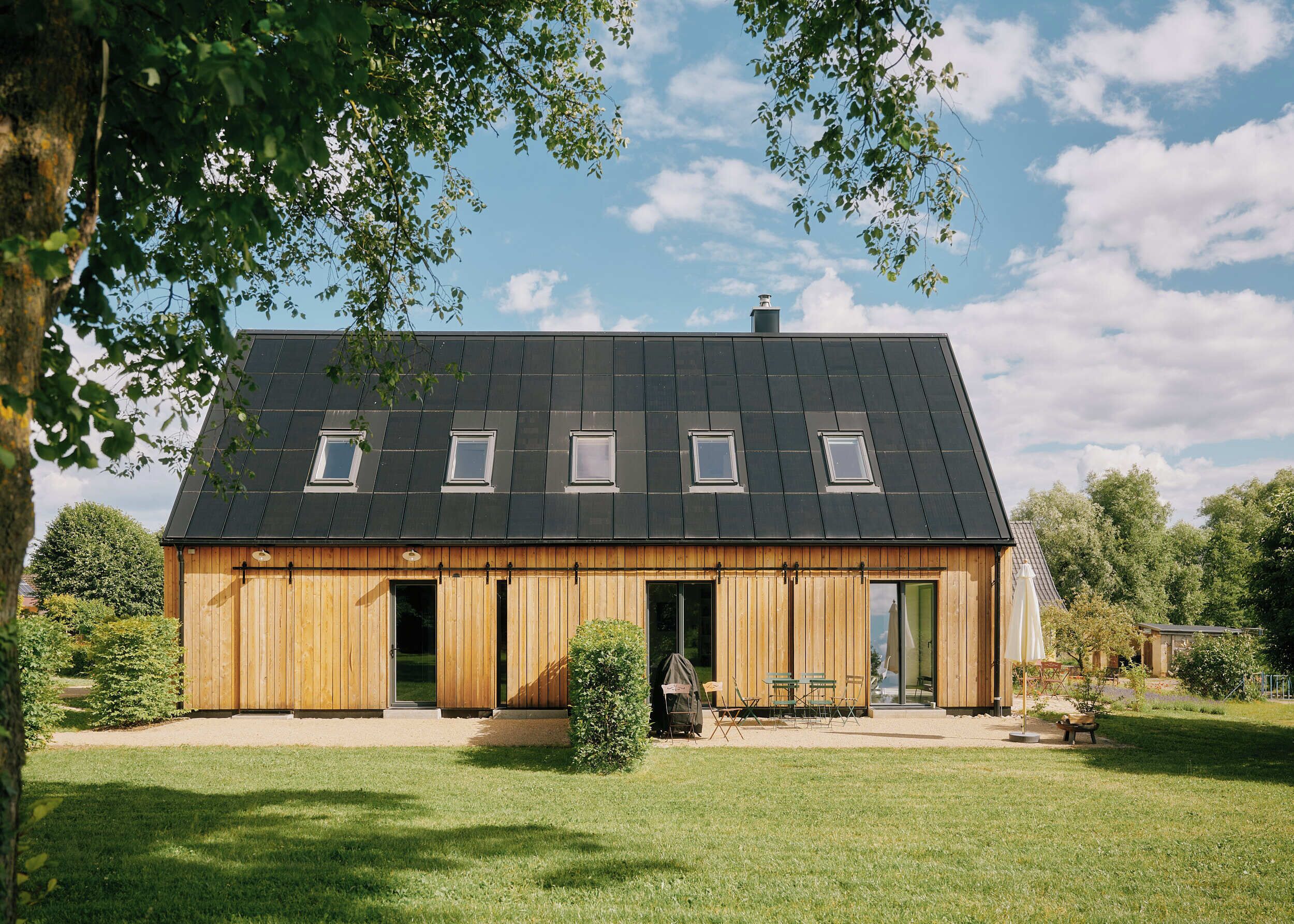 A modern wooden house with a sloped roof, multiple windows, and a large open door.
