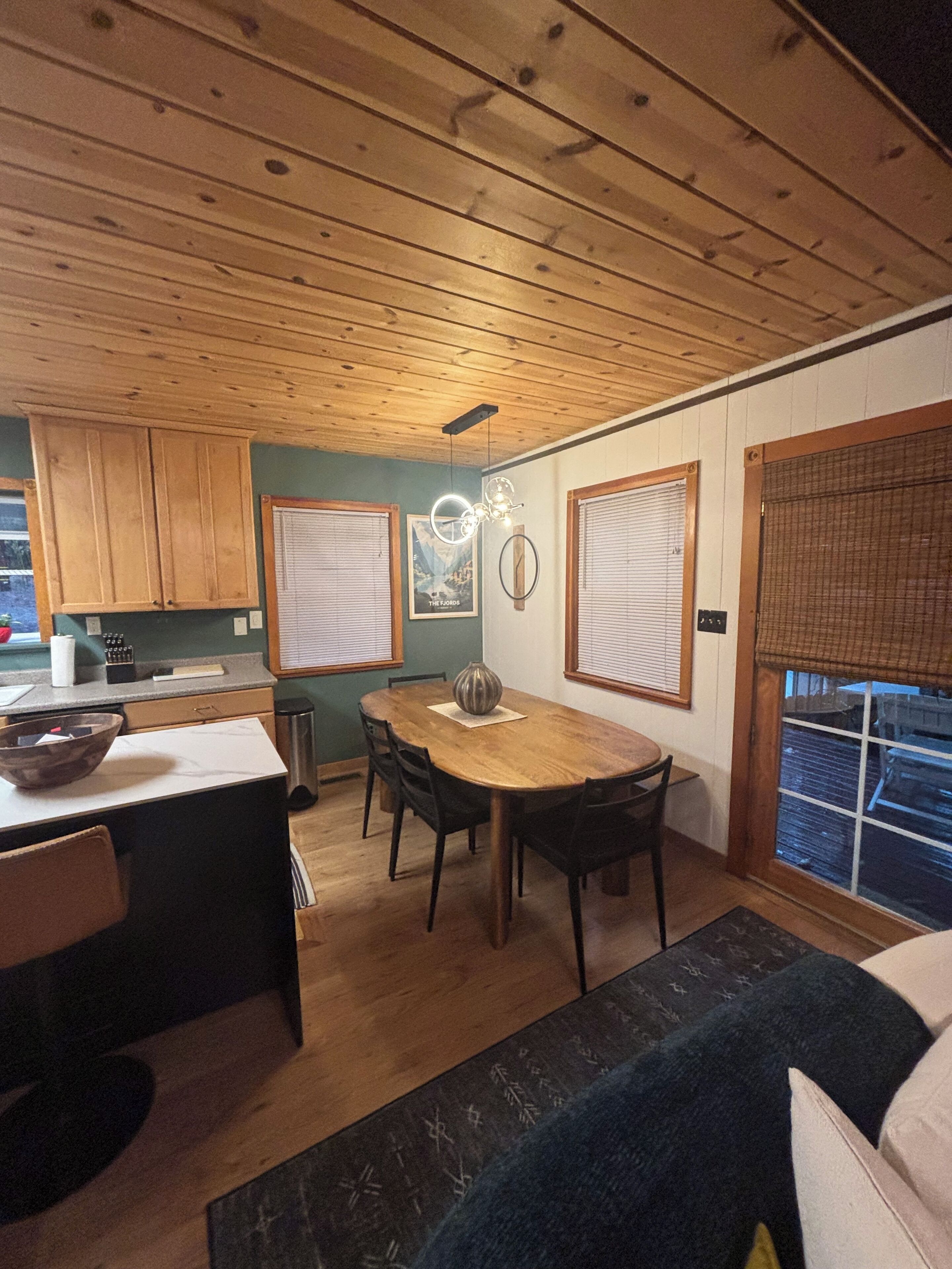 Un interior de madera con una mesa de comedor, sillas, una zona de cocina y un ventanal con persianas.