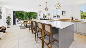 Une cuisine moderne dotée d’un grand îlot central, de tabourets de bar, de luminaires suspendus et offrant une vue sur le jardin.