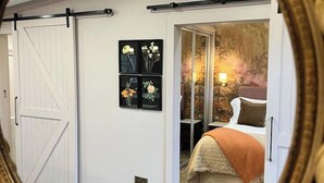 A bedroom with a sliding door, a bed with a beige blanket, a nightstand, and a wall-mounted lamp. - The Fuller's Shed All Weather Couples Rural Retreat with Private Hot tub (Dadlington)