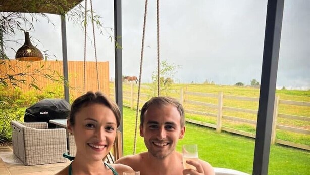 Two people in a hot tub with a view of a grassy field and a wooden fence. - The Fuller's Shed All Weather Couples Rural Retreat with Private Hot tub (Dadlington)