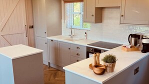 A modern kitchen with a central island, white cabinetry, and a herringbone wood floor. - The Fuller's Shed All Weather Couples Rural Retreat with Private Hot tub (Dadlington)