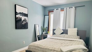 Una camera da letto con un letto, una finestra con tende, un quadro appeso al muro e una pianta su un comodino.