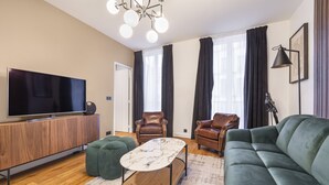 Un salon moderne avec un téléviseur à écran plat, un meuble en bois, un pouf vert, une table basse en marbre, des fauteuils en cuir et un canapé vert.