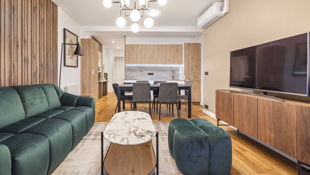 Un salon moderne avec un canapé vert, une table basse en marbre et un téléviseur posé sur un meuble en bois.