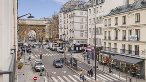 Une vue de rue avec une arche historique, des bâtiments dotés de balcons et un café avec des tables en terrasse.