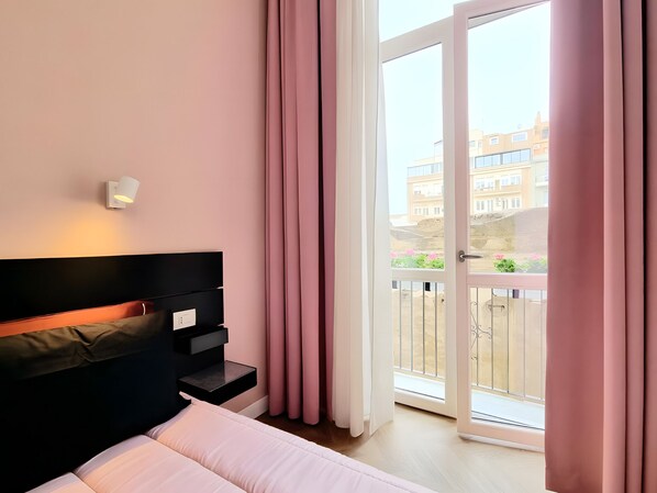 A hotel room with a bed, a nightstand, a wall-mounted lamp, and a sliding glass door leading to an outdoor balcony. - Glamor Suites by Habyto (Cagliari)