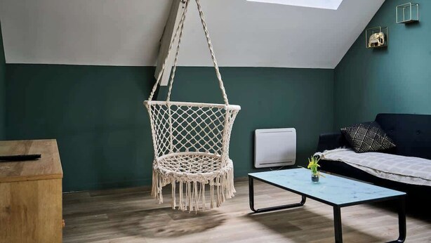 A cozy loft bedroom with a macrame chair, a small table, a dark sofa, and a skylight. - En déplacement 10, les combles wifi gratuit (Tourcoing)