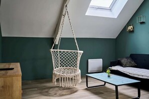 A cozy loft bedroom with a macrame chair, a small table, a dark sofa, and a skylight. - En déplacement 10, les combles wifi gratuit (Tourcoing)