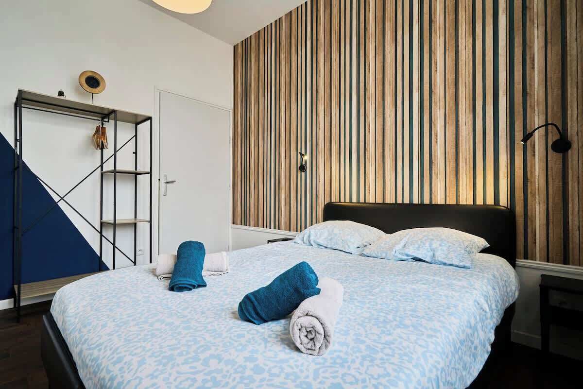 Ein Hotelzimmer mit einem Bett, einer Wand aus Holzlatten, einem Metallregal und einer blauen Wand.