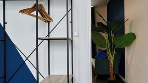 A room with a blue geometric wall, a wooden hanger rack, a small wooden table, and a large green plant. - En déplacement, Wifi, 10 minutes de la gare (Tourcoing)