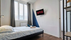 A modern bedroom with a bed, a window with curtains, a wall-mounted TV displaying 'NETFLIX', and a staircase to the right. - En déplacement, Wifi, 10 minutes de la gare (Tourcoing)