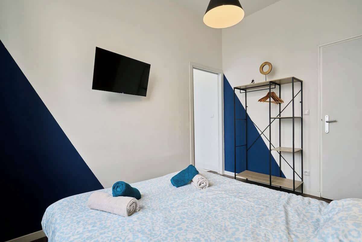 A bedroom with a bed, a TV mounted on the wall, a wardrobe, and a blue and white geometric wall design.