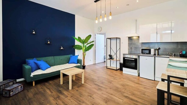 A modern apartment with a living room featuring a green sofa, a coffee table, and a potted plant. The kitchen has white cabinets, a microwave, and a stove. - En déplacement, Wifi, 10 minutes de la gare (Tourcoing)