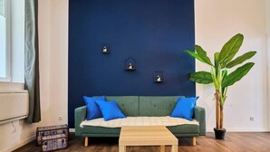 A living room with a green sofa, blue cushions, a wooden coffee table, a potted plant, and three wall-mounted lights. - En déplacement, Wifi, 10 minutes de la gare (Tourcoing)