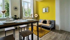 Un coin repas avec une table en bois dressée pour quatre personnes, un canapé et un mur d’accent jaune.
