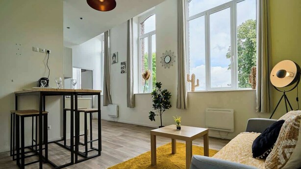 Un salon moderne comprenant un canapé, une table basse, une petite table avec une plante et un coin repas avec des tabourets.