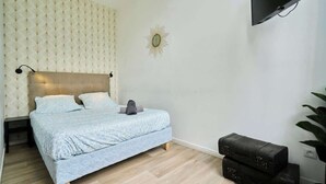 Une chambre à coucher avec un lit, une tête de lit, une horloge murale, un téléviseur et une plante.