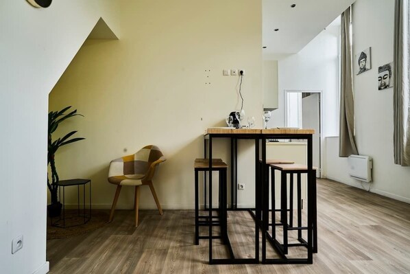 A modern living room with a wooden floor, a black metal table, a patterned chair, and a potted plant. - En déplacement 8, Wifi gratuit (Tourcoing)