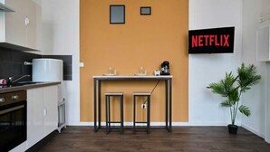 Una cucina moderna con un tavolo di legno e due sgabelli, una macchina da caffè e una TV a parete che mostra “NETFLIX”.