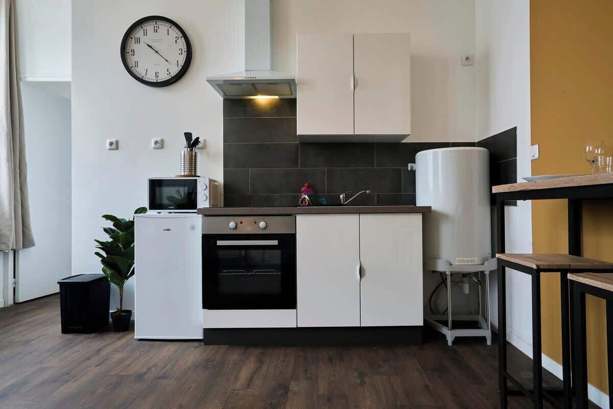 A compact kitchen with white cabinets, a built-in oven, a microwave, and a clock on the wall.