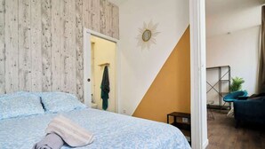 Una camera da letto con un letto, un asciugamano, una porta e vista su un'altra stanza con una sedia e una pianta.