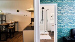 A modern kitchen with a wooden table and bar stools, a white cabinet, and a glass shower enclosure. - Modern Apt, Fast WiFi, Near Tourcoing Train (Tourcoing)