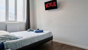 A bedroom with a bed, a window, a wall-mounted sign reading "NETFLIX," and a radiator. - Modern Apt, Fast WiFi, Near Tourcoing Train (Tourcoing)