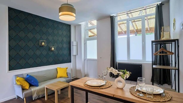 A modern living room with a sofa, a dining table set for two, and a large window with curtains. - Modern Apt, Fast WiFi, Near Tourcoing Train (Tourcoing)