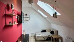 A bedroom with a sloped ceiling, skylights, a bed, a bedside table, a shelf with plants, and a mirror. - En déplacement 9, Dernier étage, wifi gratuit (Tourcoing)