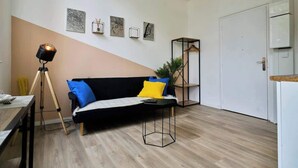 A modern living room with a sofa, a coffee table, a tripod lamp, and wall art. - Modern Apt Near Tourcoing Sta. w/ Fast WiFi (Tourcoing)