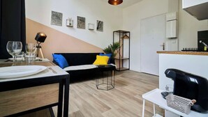 A modern living space with a dining area, a sofa with cushions, a hanging light fixture, and artwork on the wall. - Modern Apt Near Tourcoing Sta. w/ Fast WiFi (Tourcoing)