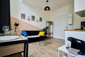 Un espace de vie moderne comprenant un coin repas, un canapé avec des coussins, un luminaire suspendu et des œuvres d’art accrochées au mur.