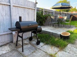 Una parrilla, mobiliario de exterior y una zona de patio con valla de madera y vegetación.