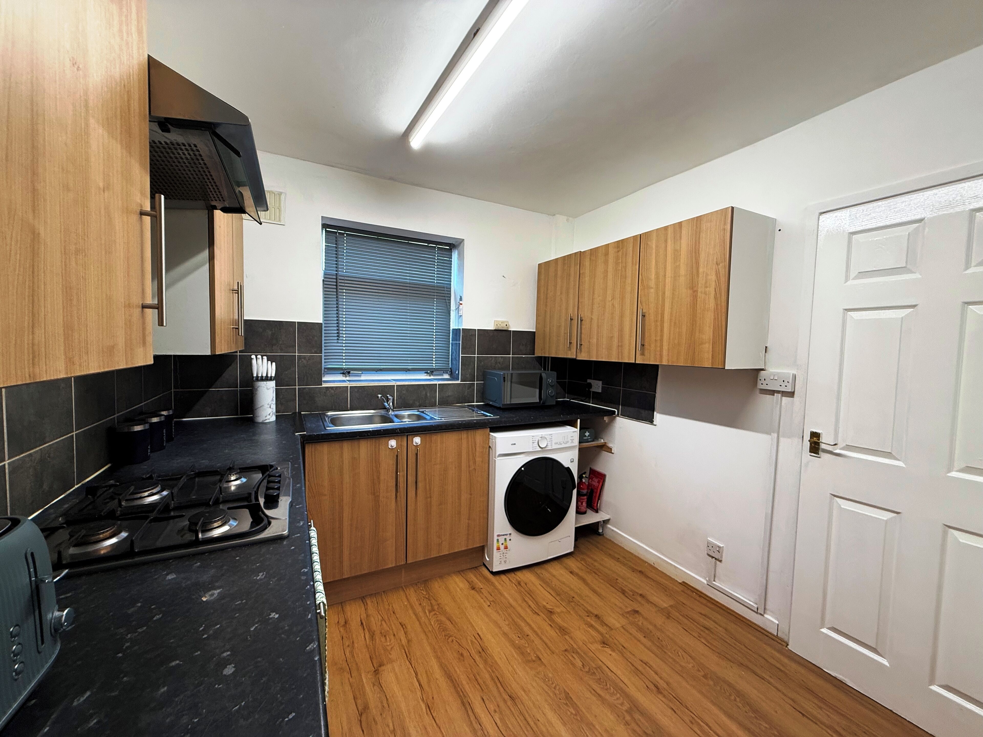 A compact kitchen with a gas stove, a washing machine, and a microwave.