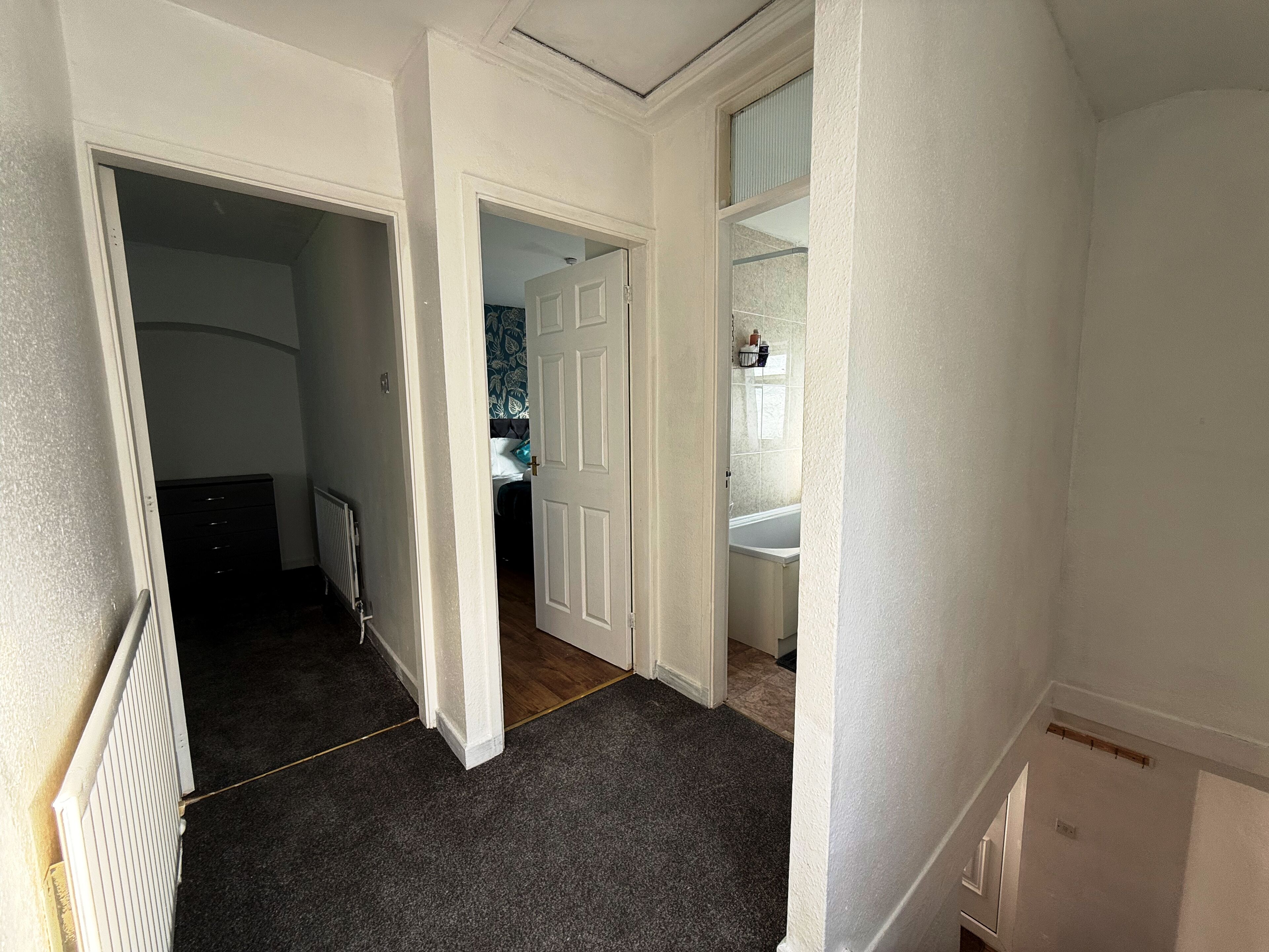 A hallway with a radiator, a door leading to a bedroom, and a bathroom with a sink and mirror.