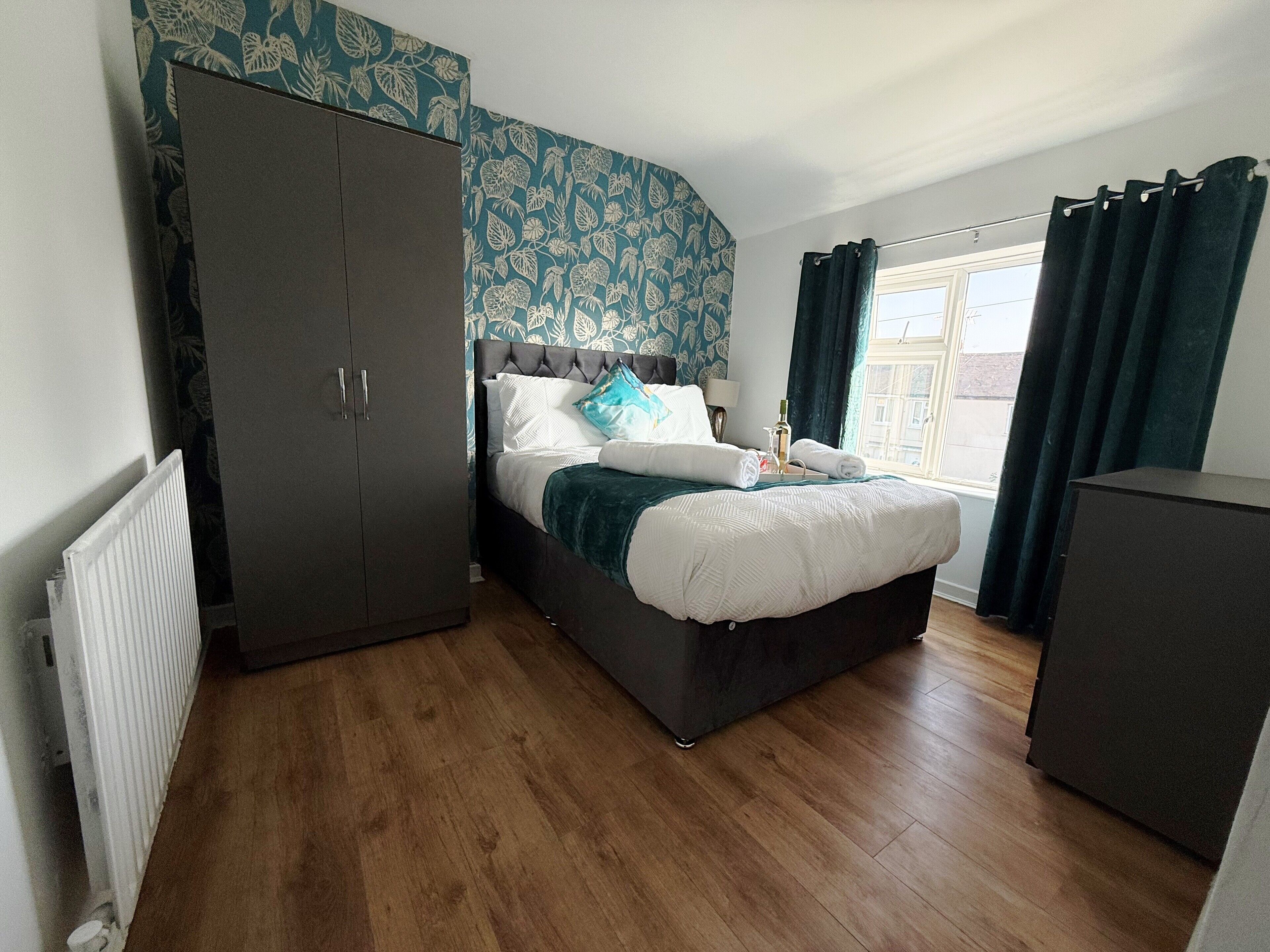 Ein Schlafzimmer mit Bett, Kleiderschrank, Heizkörper und einem Fenster mit Vorhängen.