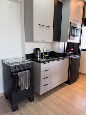 A compact kitchen with a gas stove, oven, microwave, and a small refrigerator.